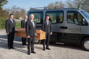 Porteurs funéraires en costume posant devant un véhicule avec un cercueil.