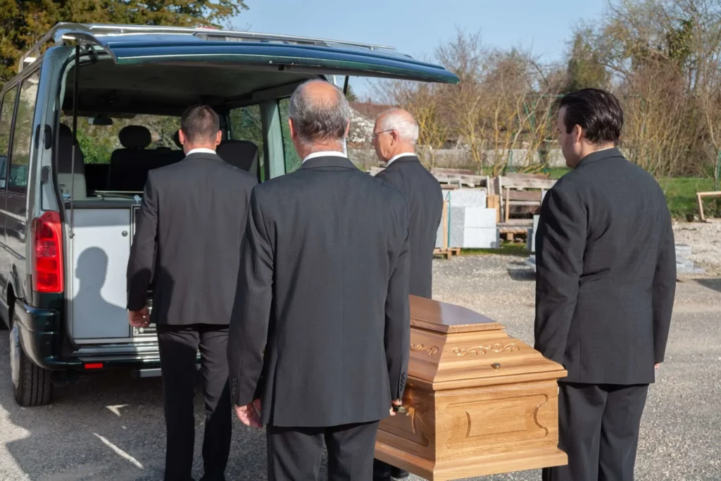 Porteurs funéraires transportant un cercueil vers l'arrière d'un corbillard.