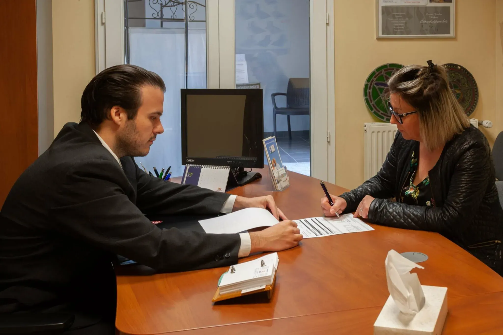 Entretien individuel entre un conseiller funéraire et une cliente en bureau.